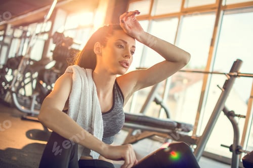 Preview: Tired and exhausted female athlete sitting on floor at gym.