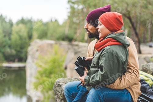 Preview: side view of father and smiling son with binoculars looking away in autumn forest