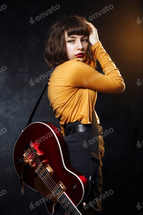 Preview: Serious young hipster woman with curly hair with red guitar in neon lights.