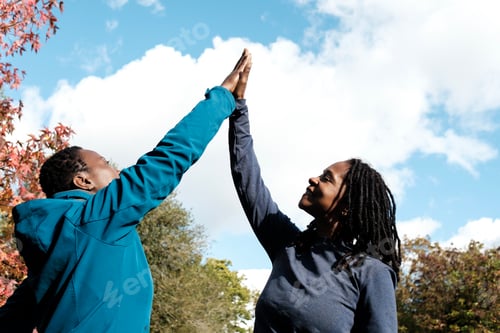 Preview: Two black mature fitness women making high five outdoors.