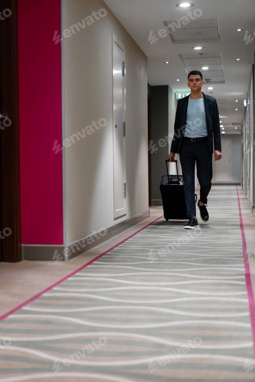 Preview: A man with a suitcase walks down the hotel corridor a view of a businessman on trip