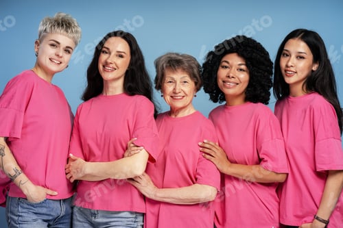 Preview: Five diverse women wearing pink t shirts are smiling and posing together
