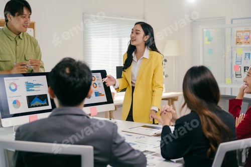 Preview: Asian businesswoman leading meeting with team using charts on computer monitors