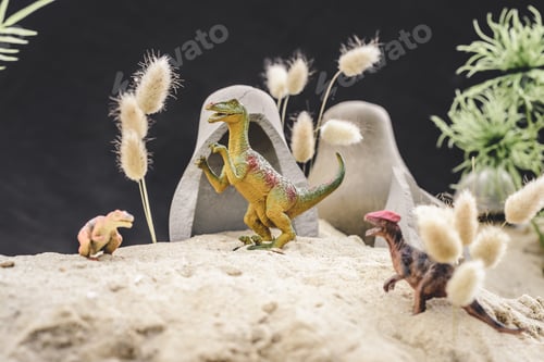 Preview: selective focus of toy dinosaurs standing near caves and plants on sand dune