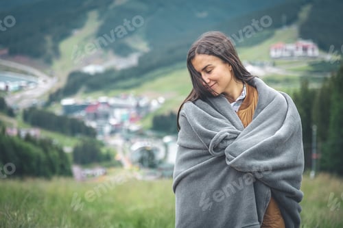 Preview: A young woman wrapped in a blanket in the mountains.