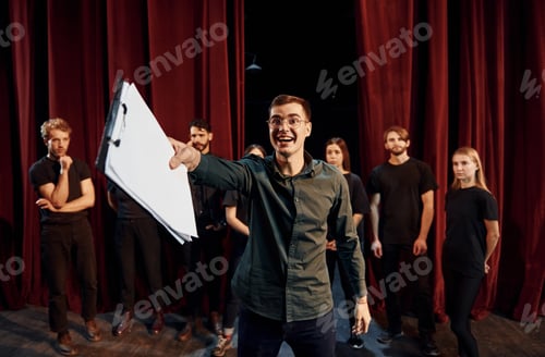 Preview: Man is practicing his role. Group of actors in dark colored clothes on rehearsal in the theater
