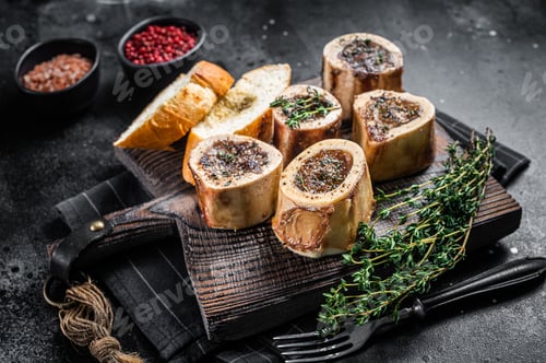 Preview: Roast marrow calf bones on wooden board with bread and herbs. Black background. Top view