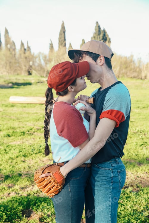 Preview: Young couple with baseball equipment kissing in park