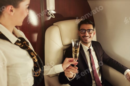 Preview: Young business man travelling first class, flight attendant is bringing him glass of champagne