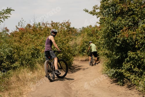 Preview: Two cyclists riding on a dirt trail surrounded by lush green foliage