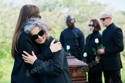 Preview: Young grieving woman giving hug to her mourning mother in sunglasses
