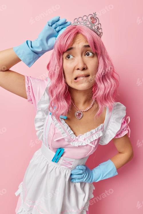 Preview: Worried housemaid bites lips looks unhappily looks away wears crown white dress and rubber gloves fe