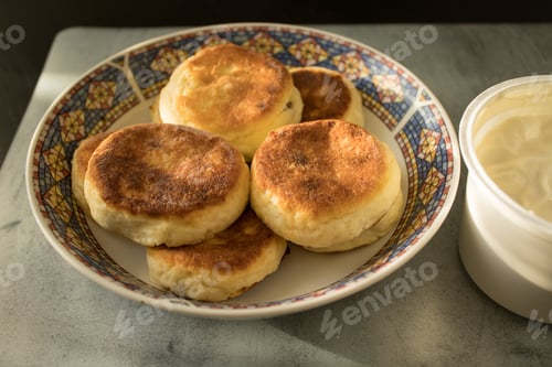 Preview: A plate with cheese pancakes next to sour cream on a marble mat on a black wooden table.