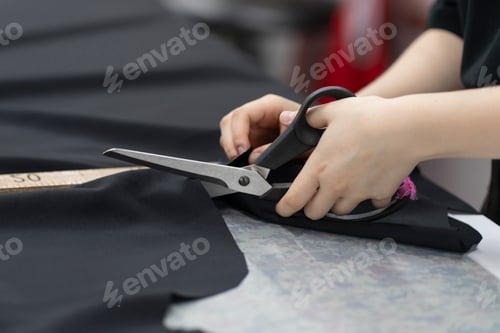 Preview: a female tailor cutting fabric with scissors in the office