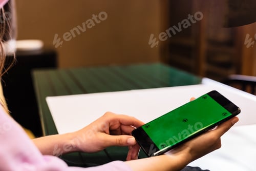 Preview: Woman holding smartphone with green screen in restaurant