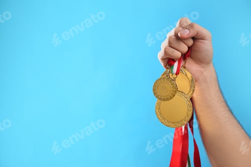 Preview: Man holding golden medals on light blue background, closeup. Space for design
