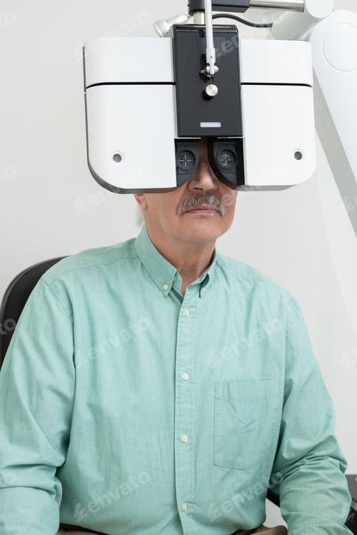 Preview: Senior male patient looking through lens of ophthalmological equipment