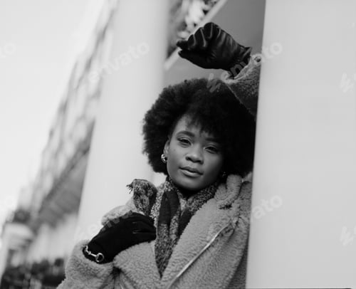 Preview: Black and white portrait of black woman leaning on building columns.