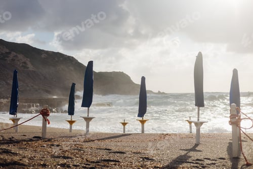 Preview: Closed umbrella on sardinia beach at sunset with rough sea