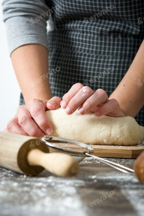 Preview: Baker kneading dough on wooden table with rolling pin and flour