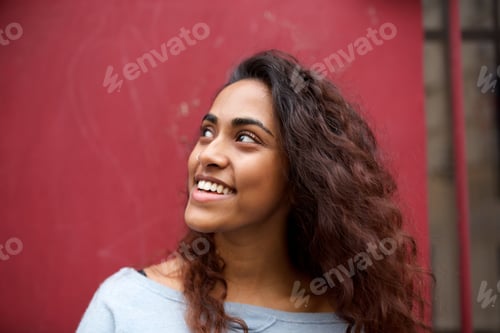 Preview: beautiful young Indian woman smiling and looking away against red background