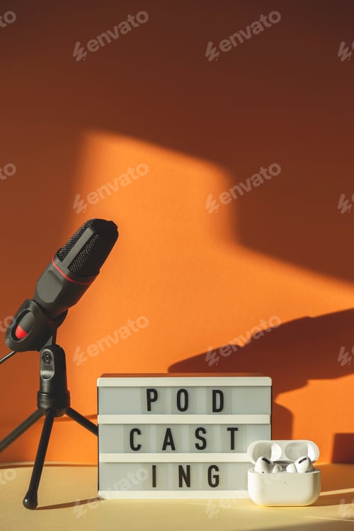 Preview: Podcasting lettering next to microphone and wireless headphones at workplace in hard shadows
