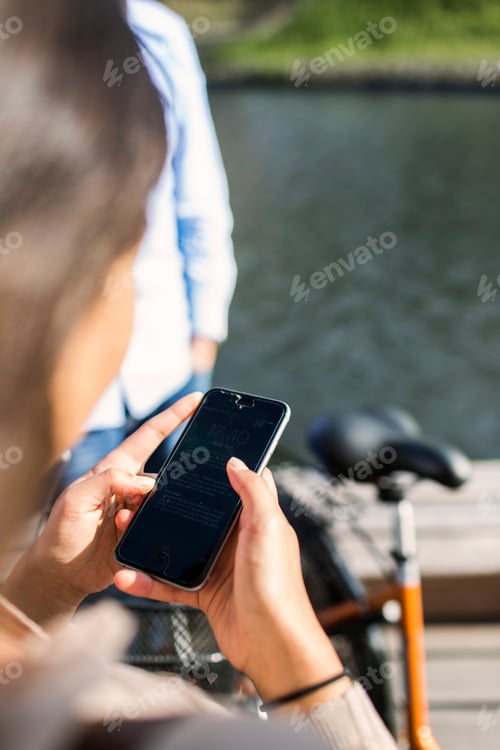 Preview: Rear view of young woman using smart phone by canal on sunny day