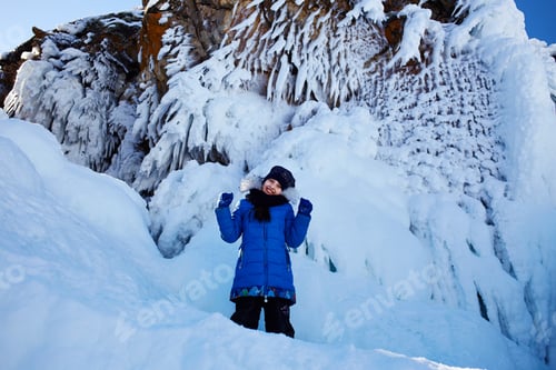 Preview: A joyful girl stands by the snowy rock.