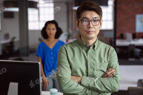 Preview: Portrait of serious asian businessman standing in office with female colleague in background