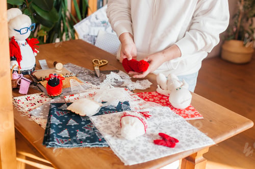 Preview: female hands make handmade dolls on the background of multicolored fabric, scissors