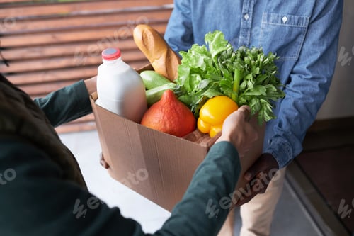 Preview: Close up of delivery man handing bag with fresh groceries to client