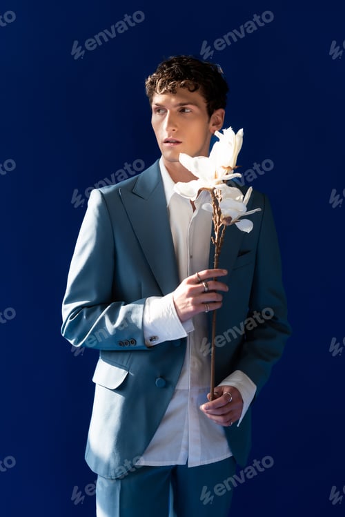 Preview: Stylish man in suit and shirt holding magnolia branch isolated on navy blue