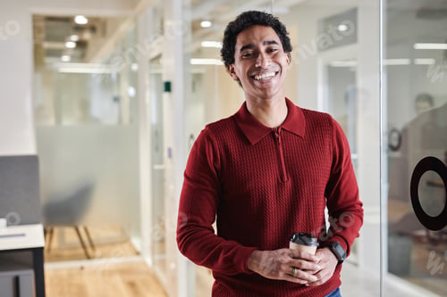 Preview: Young Arabian man holding coffee cup standing by glass wall in office