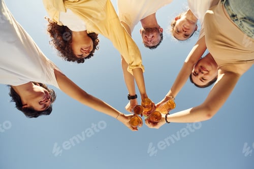Preview: Upside down. View from below of people that are cheering with beer bottles