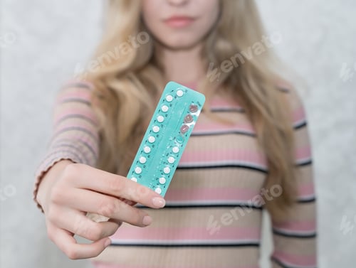 Preview: girl holding a blister of oral contraceptives in her hand, soft focus, women's health