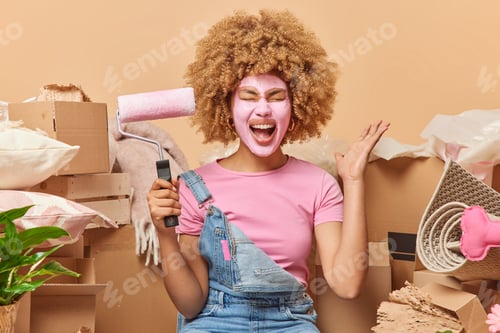Preview: Emotional curly haired woman exlaims loudly keeps palm raised holds paint roller redecorates new apa
