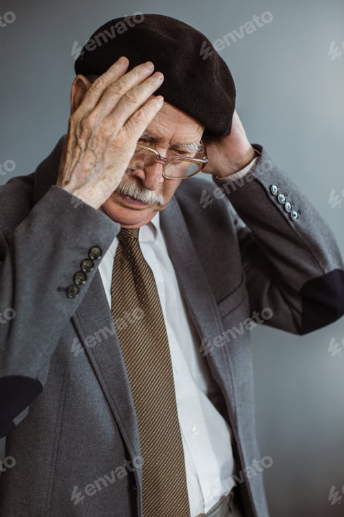 Preview: Gray-haired man in his 80s puts on a hat while standing in the living room at home.