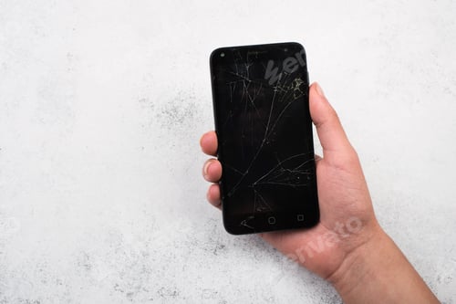 Preview: Closeup shot of a person's hand holding a cracked smartphone against a rusty wall background