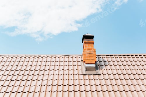 Preview: Tiled roof of a house with a brick chimney against a blue cloudy sky during the day. Exterior of a