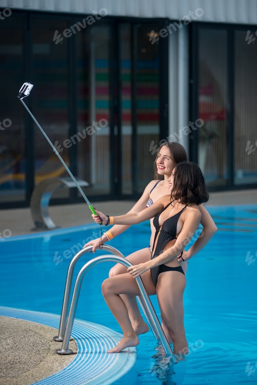 Preview: Two happy beautiful girls in swimsuits posing against the swimming pool.