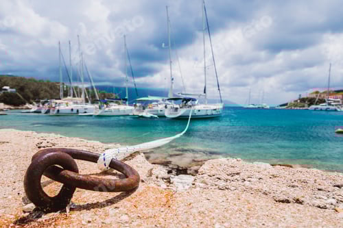 Preview: Mooring rope tied to rusty ring for rigging yachts in background. Wonderful view of port Fiskardo