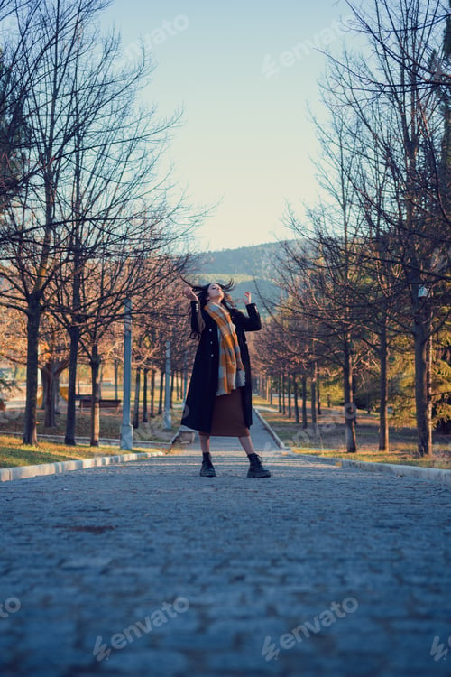 Preview: Woman in an overcoat and scarf walks through an autumn park at dusk