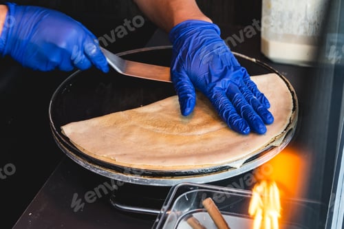 Preview: High angle shot of a person with blue gloves making delicious crepe