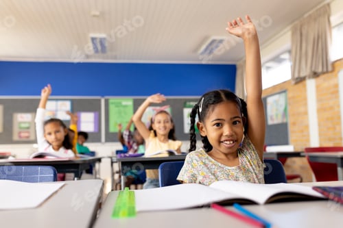 Preview: Portrait of happy biracial school girl raising her hand in classroom at elementary school