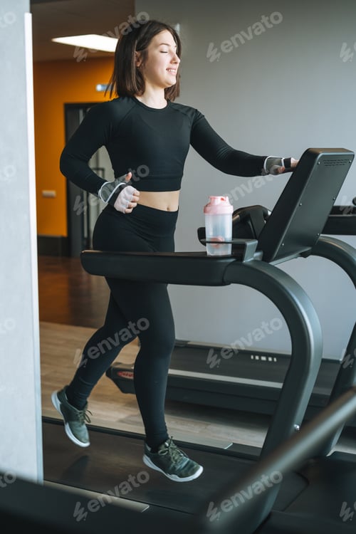 Preview: Young fitness brunette woman training for cardio equipment at gym