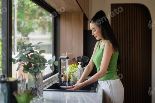 Preview: Asian woman washing dishes in the kitchen sink at home