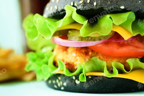 Preview: Macro view of tasty black burger with beef, cheese, lettuce, onion, tomatoes on blue background