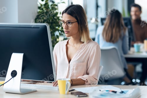 Preview: Beautiful young business woman working with computer while sitting in desk in modern startup office.