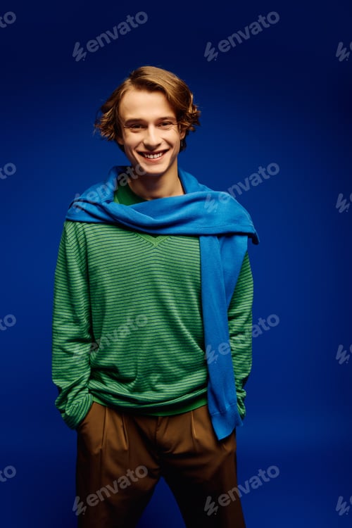 Preview: Young man embraces modern youth culture with striking fashion in vibrant blue backdrop