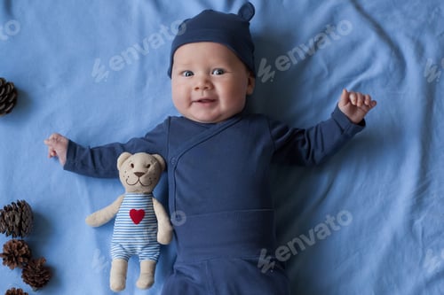 Preview: baby boy 3 months lies and smiles and holds a small toy bear in his hands.